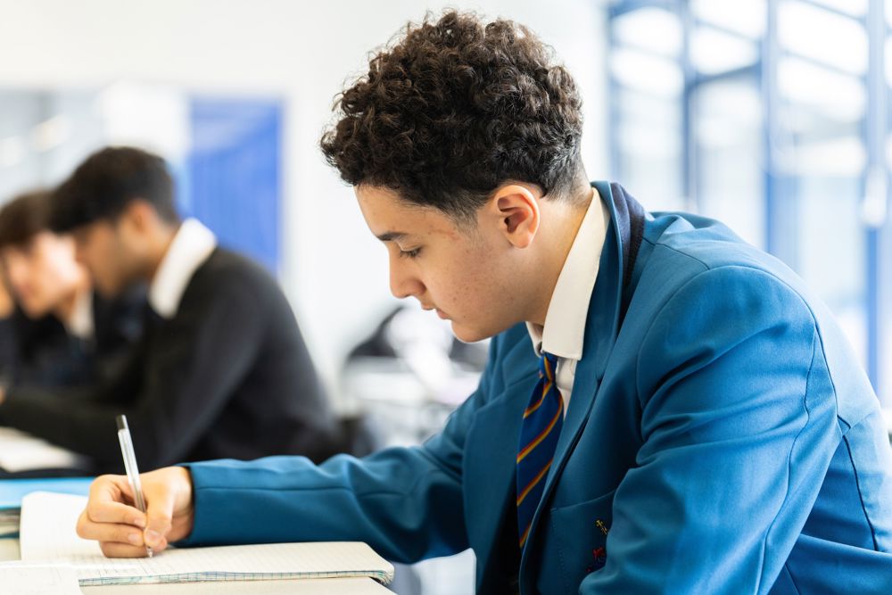 Pupil working at a desk, writing in an exercise book